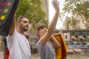 retrato de um jovem casal caucasiano alegre homem e mulher segurando muitos sacos de papel depois de fazer compras enquanto caminhava e conversava na rua. casal de família feliz com pacotes ao ar livre. conceito de compra foto