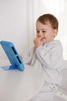 menino feliz jogando jogo no tablet digital em casa. retrato de uma criança em casa assistindo desenho animado no tablet. criança moderna e tecnologia educacional. foto