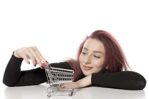 mulher feliz segurando cartões de crédito e um pequeno carrinho de compras vazio isolado no fundo branco foto