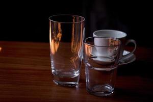 copos de água de vidro transparente e canecas de café colocadas sobre uma mesa de madeira. foto