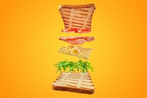 sanduíche fresco com ingredientes voadores em fundo amarelo isolado foto