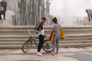 retrato de um jovem casal caucasiano alegre homem e mulher segurando muitos sacos de papel depois de fazer compras enquanto caminhava e conversava na rua. casal de família feliz com pacotes ao ar livre. conceito de compra foto