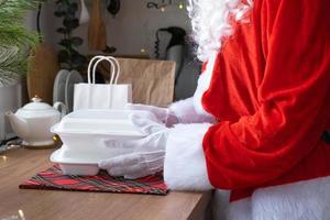 entrega de comida para recipientes de serviço doméstico nas mãos do papai noel coloca na mesa da cozinha e leva embora. pedido quente pronto, natal, restauração de feriados de ano novo. foto