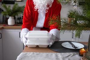 entrega de comida para recipientes de serviço doméstico nas mãos do papai noel coloca na mesa da cozinha e leva embora. pedido quente pronto, natal, restauração de feriados de ano novo. foto