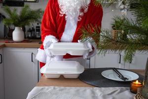 entrega de comida para recipientes de serviço doméstico nas mãos do papai noel coloca na mesa da cozinha e leva embora. pedido quente pronto, natal, restauração de feriados de ano novo. foto