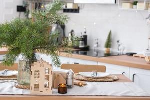 decoração festiva de natal na cozinha branca, café da manhã festivo, interior scandi branco. a figura de uma casa aconchegante na mesa posta. ano novo, humor, casa aconchegante. copie o espaço foto