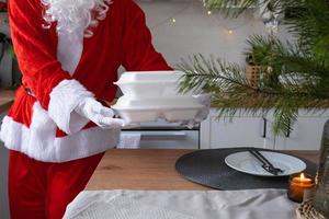 entrega de comida para recipientes de serviço doméstico nas mãos do papai noel coloca na mesa da cozinha e leva embora. pedido quente pronto, natal, restauração de feriados de ano novo. foto