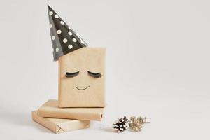 caixas de presente com papel kraft em fundo cinza, decoração de presente original com cílios postiços e chapéu de festa, minimalista foto