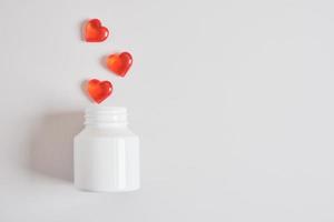 pílulas vermelhas em forma de coração e frasco branco. símbolo do amor. pílulas de amor. pílulas para a saúde do coração. foto