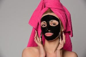 bela modelo feminino com máscara cosmética facial preta. isolado em fundo cinza foto