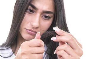 retrato da bela jovem triste com cabelo comprido na mão. close-up do modelo feminino infeliz olhando para o cabelo com pontas duplas. conceito de cuidado de cabelo foto