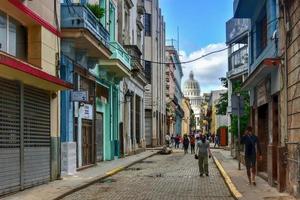 havana, cuba - 8 de janeiro de 2017 - pessoas andando pelas ruas da velha havana com o edifício da capital nacional ao fundo. foto