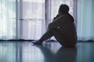 esquizofrenia com solitário e triste no conceito de depressão de saúde mental. mulher deprimida sentada contra o chão em casa com quarto escuro sentindo-se miserável. as mulheres estão deprimidas, medrosas e infelizes. foto