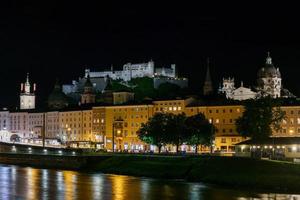 vista noturna da cidade de salzburgo. catedral, cidade velha altstadt, evangelische pfarrgemeinde christuskirche hohensalzburg castelo iluminado à noite. passeio marítimo do rio salzach em salzburgo, áustria. foto