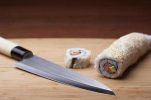 sushi e faca em uma tábua de corte de madeira foto