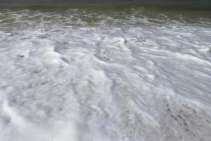 espuma de água com areia lisa. ondas na costa da bela praia de areia tropical em um dia ensolarado foto