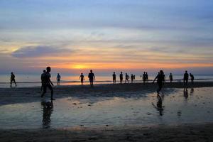 viajar para a ilha koh chang, tailândia. os meninos estão jogando futebol na praia no fundo do pôr do sol colorido. foto