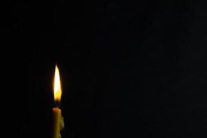 um close-up de uma vela acesa com chama amarela, uma luz de vela no escuro, ela queima e depois de um tempo uma rajada de vento a apaga. foto