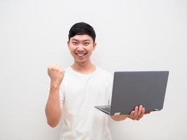 camisa branca de homem asiático segura laptop na mão e punho com sorriso feliz no rosto onm fundo branco foto