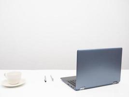 laptop com xícara de café e caneta na mesa de trabalho no quarto fundo branco foto