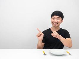 homem asiático sorrindo, sente-se à mesa com o dedo apontador de talheres no espaço da cópia foto