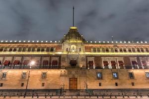 palácio nacional iluminado na plaza de la constitucion da cidade do méxico à noite. foto