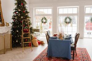 decoração de natal na sala de estar com grandes janelas, mesa de jantar e árvore de natal foto