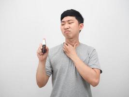 homem asiático sentindo dor de garganta e olhando para spray de garganta na mão foto