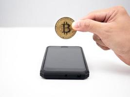 homem segurando bitcoin acima do celular na mesa foto
