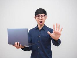 homem asiático de óculos segurando laptop e mostra a mão para parar com rosto sério fundo branco foto
