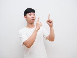 homem asiático camisa branca rosto alegre aponte o dedo duplo para cima e olhe para cima no fundo branco foto