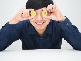 homem asiático rosto sorridente alegre closeu seus olhos por ouro bitcoin sentado à mesa foto