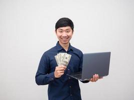 homem asiático ganha dinheiro e segurando laptop na mão sorriso feliz no fundo branco foto