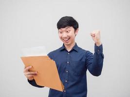 homem asiático lendo no envelope do documento na mão, sentindo-se feliz e sorrindo, mostra o punho para cima fundo branco foto