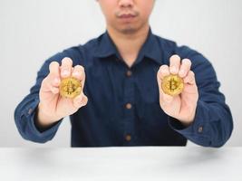 homem sentado à mesa e mostrando bitcoin dourado na mão foto