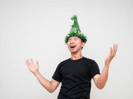 homem asiático camisa preta com chapéu verde alegre no rosto mostra a mão para cima e olha para cima na celebração de fundo branco feliz conceito de ano novo foto