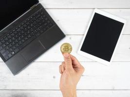 mão segurando ouro bitcoin com laptop e tablet na vista superior do plano de fundo da mesa foto