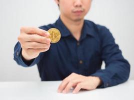 homem sentado à mesa e mostrando ouro bitcoin na mão foto