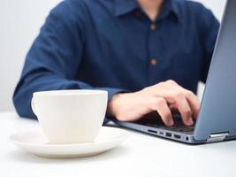 foto de corte de homem usando laptop e xícara de café na mesa