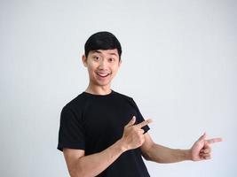 homem asiático alegre aponta o dedo duplo para o lado direito no retrato de fundo de parede branca