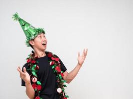 homem asiático camisa preta com chapéu verde e borla colorida alegre no rosto mostra a mão para cima e olha para cima na celebração de fundo branco feliz conceito de ano novo foto