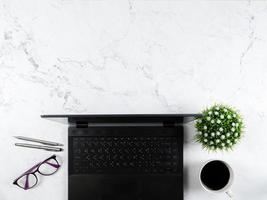 fundo de mármore de mesa de área de trabalho de vista superior, tela preta de smartphone no laptop de teclado com caneta de prata de óculos e espaço de cópia de xícara de café acima foto