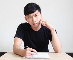 jovem asiático falando com telefone cara séria segurando a caneta e a prancheta na mesa olhe para a câmera, registre o conceito de trabalho foto