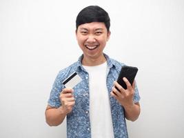 homem camisa azul furando cartão de crédito e telefone inteligente se sente feliz rosto satisfeito foto