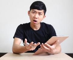 homem asiático, sente-se à mesa, segurando a caneta e a prancheta na mão, olhe para o rosto confuso da câmera no branco isolado, registre o conceito de trabalho foto