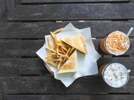 francês frito com sanduíche em placa de madeira café da manhã com chá tailandês e leite de café branco no espaço de exibição de mesa de madeira no café