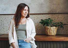 mulher sorridente morena adulta de meia-idade amigável cinquenta anos na camisa branca com uma xícara de café da manhã na cozinha em casa foto