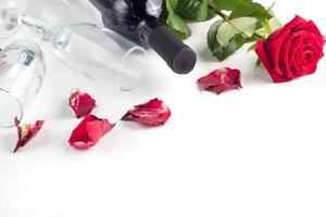 garrafa de vinho, vidro e rosa vermelha com pétalas em um fundo branco foto