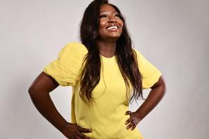 feliz mulher de pele escura em vestido de moda amarelo. modelo afro-americano de beleza posando em estúdio isolado em fundo cinza foto