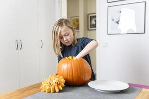 lindo menino loiro esculpindo abóbora com faca para o halloween. conceito de halloween foto